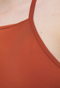 Débardeur couleur rouille avec des fines bretelles, présentant une texture lisse et mate ainsi qu'un subtil détail de couture le long de l'encolure et des emmanchures.