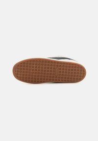 Semelle de chaussure avec une bande de roulement en caoutchouc brun présentant une grille de formes en losange en relief et un petit logo rectangulaire au centre.