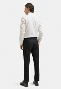 Vit långärmad skjorta med krage, kombinerad med svarta byxor med bakfickor och en skräddarsydd passform. Svarta skor.