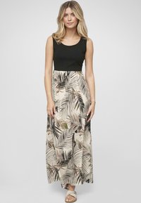 Robe maxi avec un corsage en débardeur noir et une jupe crème à motifs arborant des feuilles de palmier vertes et brunes. Tissu léger, design fluide.