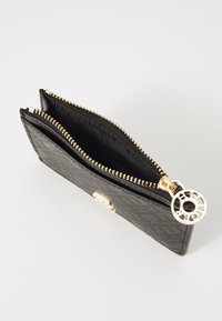 Portafoglio nero con zip realizzato in pelle texturizzata, dotato di accessori in oro e un portachiavi decorativo. Ha due scomparti per l'organizzazione.