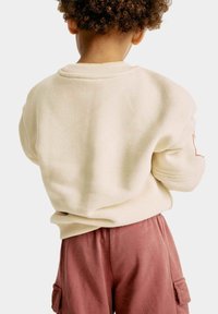 Krämfärgad sweatshirt med strukturerad yta, ribbad krage och uppvikta ärmar, kombinerad med rosa cargoshorts med sidofickor.