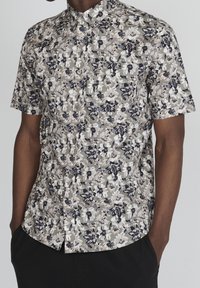 Koszula z krótkim rękawem, zapinana na guziki, w kwiatowy wzór, prezentująca białe, granatowe i szare kwiaty na stonowanym tle. Posiada kieszeń na piersi.