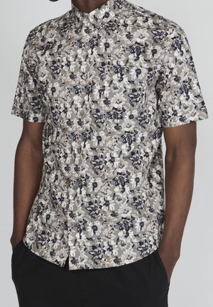 Camisa de manga corta con botones en un estampado floral, que presenta flores en blanco, azul marino y gris sobre un fondo atenuado. Incluye un bolsillo en el pecho.