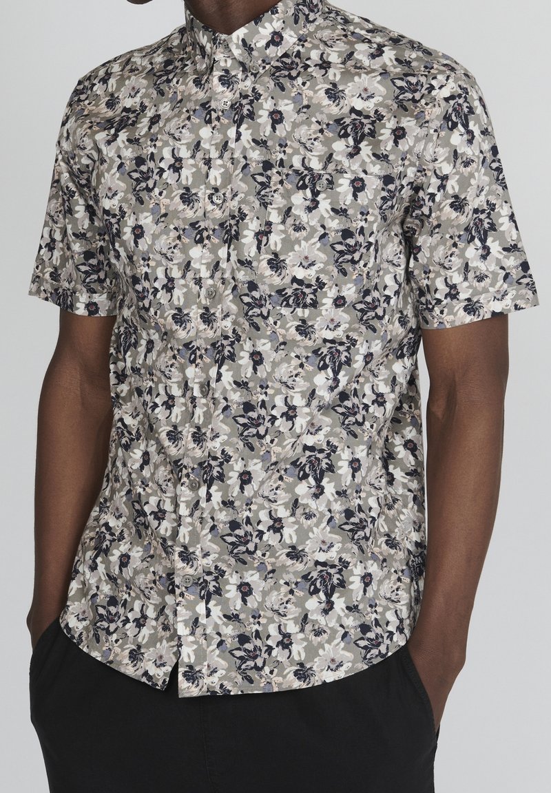Koszula z krótkim rękawem, zapinana na guziki, w kwiatowy wzór, prezentująca białe, granatowe i szare kwiaty na stonowanym tle. Posiada kieszeń na piersi.