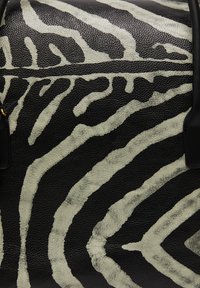 Sort læder håndtaske med cremefarvede zebra-striber, struktureret finish og sorte metaldele. Inkluderer et mærke hængende fra siden.