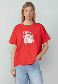 Rode katoenen T-shirt met korte mouwen, voorzien van een grafische print van een citroen en de tekst "JOUW DAGELJKSE VITAMINE" in het wit.