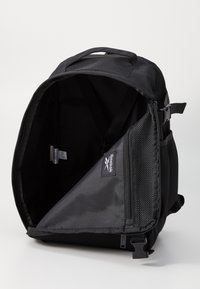 Črn nahrbtnik s širokim odpiranjem, notranjim mrežastim žepom, gladkim materialom in logotipom Reebok. Ima nastavljive naramnice in zgornjo ročico.