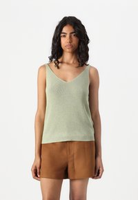 Lys grønn ermeløs topp med v-hals, med ribbestruktur og en tettsittende design, kombinert med brune shorts.