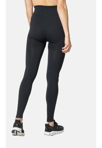 Zwarte geribbelde leggings met een hoge tailleband, die een gladde textuur en een aansluitend ontwerp laten zien, gecombineerd met zwarte sportschoenen.