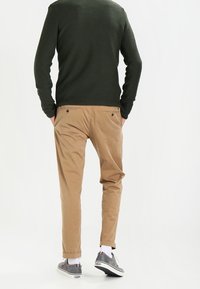 Chino beige con vestibilità rilassata, abbinati a un maglione texture verde scuro e scarpe grigie. Design semplice senza motivi visibili.
