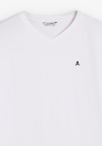 T-shirt bianca in cotone con scollo a V, caratterizzata da un piccolo logo di teschio e tibie nero sul lato sinistro del petto. Texture liscia, vestibilità standard.