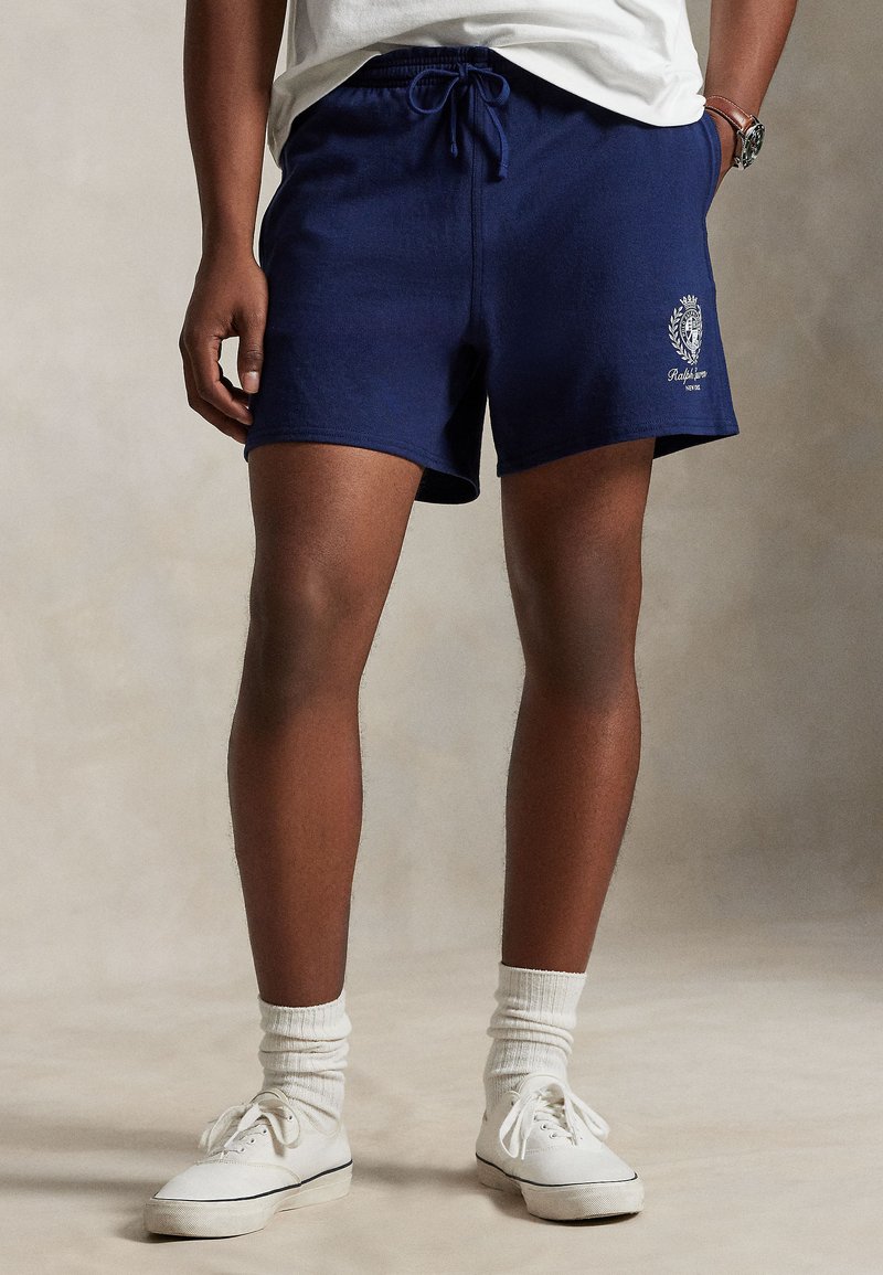 Marineblå badebukser med snor i livet, mykt bomullsmateriale og brodert logodetalj på venstre ben. Brukes med hvite joggesko og sokker.