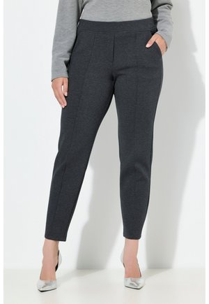 Grijze, rekbare, taps toelopende broek met zijnaaddetails en elastische tailleband. Gemaakt met een lichtgrijze top en zilveren hakken tegen een effen achtergrond.