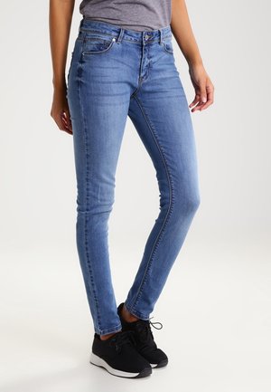 Jeans skinny azzurri chiari in denim, con cinque tasche, passanti per la cintura e bottone di chiusura. Indossati con scarpe sportive nere.