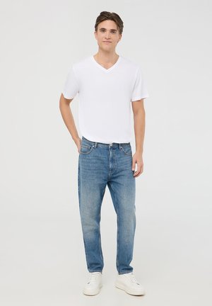 T-shirt bianca a maniche corte con scollo a V abbinata a jeans dritti blu chiaro e sneaker bianche, che mostrano un outfit casual.