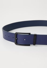 Marineblå lærbelte med en glatt tekstur, med en svart metalspenne og flere hull for justering.