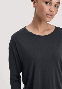 Dunkelgraues Langarmshirt mit Rundhalsausschnitt und lockerer Passform. Hergestellt aus weichem Stoff, mit dezentem Fall und ohne sichtbare Muster.