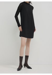 Svart långärmad klänning med vertikala ränder, rund halsringning och lös passform. Kombinerad med genomskinliga svarta strumpor och svarta klackskor med spetsig tå.