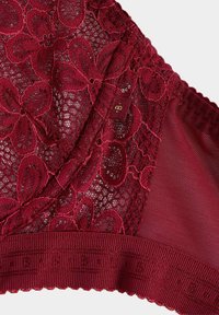 Nahaufnahme roter Spitzenunterwäsche mit Blumenmustern, Netzstoff und einem elastischen Bund, der ein kleines Größenschild zeigt.