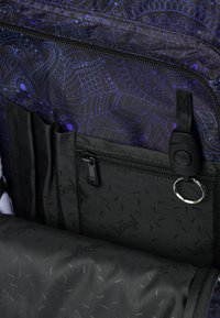 Interno della borsa a motivo nero e viola con tasche, cerniere e un anello metallico; texture liscia con design geometrici.