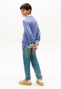 Pullover azzurro chiaro lavorato a maglia con motivo a treccia, indossato sopra una camicia bianca con colletto. Combinato con jeans blu sbiaditi e sneakers beige.