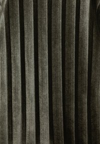 Tessuto plissettato verde scuro con una texture vellutata e accenti metallici. Strisce verticali creano un aspetto strutturato ma morbido.