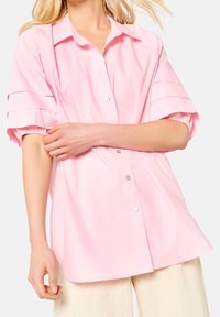 Pink oversized button-up shirt with short, gathered sleeves and subtle horizontal stripes. Made of smooth, lightweight fabric.