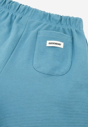 Hellblaue Shorts aus strukturiertem Stoff, mit einem elastischen Bund und einer aufgesetzten Tasche mit einem Etikett, das "GOODBOIS" liest.