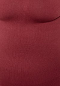 Mörkröd tanktopp i ribbat tyg med en åtsittande design. Slät textur, rundad halsringning och inga synliga knäppningar eller dekorationer.
