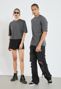 Grå bomull t-shirts, avslappnad passform, bärs med svarta shorts. Setet inkluderar svarta kängor och slitna svarta jeans. Minimalistisk design.