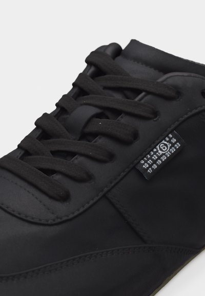 Μαύρο αθλητικό παπούτσι με μαύρα κορδόνια, μαλακό επενδυμένο περιλαίμιο και μικρή ετικέτα στο πλάι που δείχνει αριθμούς μεγέθους σε λευκό χρώμα.