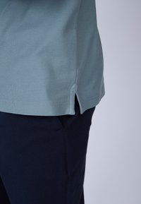 Chemise bleu clair à manches courtes en tissu texturé, avec des fentes latérales à l'ourlet, assortie à un pantalon noir marine.