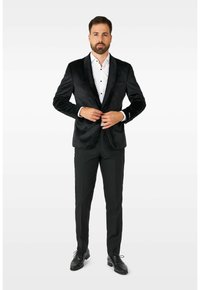 Črni žametni smoking z satenskimi reverji, oblečen čez belo srajco z črnimi gumbi, v kombinaciji s črnimi hlačami in sijočimi črnimi čevlji.