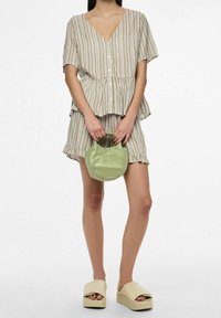 Top a righe con maniche corte e scollatura a V, con bottoni, abbinato a una gonna arricciata coordinata. Tiene una borsa verde texturizzata; indossa scarpe con plateau beige.