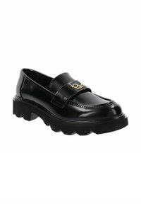 Mocassin en cuir verni noir avec une semelle en caoutchouc épaisse, présentant un accent en métal doré sur la sangle et des détails cousus le long des côtés.