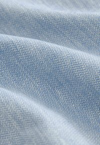 Tissu bleu clair présentant un motif chevron, avec une texture lisse et un léger éclat, plié pour montrer la profondeur et la dimension.