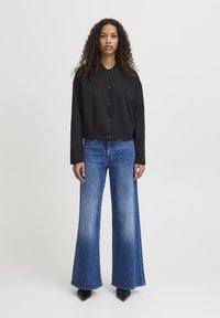 Black cropped button-up jacket with long sleeves paired with light blue flared jeans. The jeans feature a faded texture and wide leg openings.