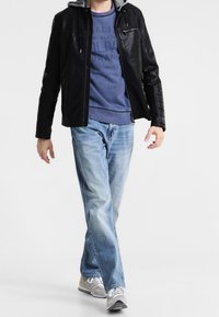 Veste en cuir noire avec un sweat à capuche gris en dessous, associée à un jean bleu clair et des baskets grises, présentant une tenue décontractée.