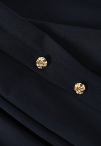 Tissu marine à texture lisse, avec deux boutons ronds dorés texturés sur une section pliée. Design simple aux lignes épurées.