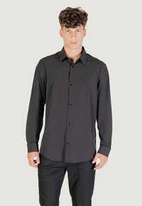Camicia nera a maniche lunghe con bottoni realizzata in tessuto morbido, con colletto classico, chiusura anteriore con bottoni e design aderente con orlo curvo.