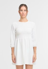 Witte jurk met een textuur op het lijfje, lange, pofmouwen en een losse pasvorm. Glad materiaal met een geplooide taille en een lengte tot de knie.