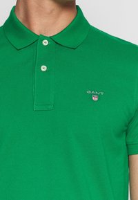 Polo verde realizzata in cotone, dotata di colletto classico, due bottoni e logo ricamato sul petto sinistro. La texture è liscia.