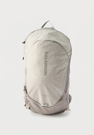 Ανοιχτό γκρι σακίδιο πλάτης Salomon Trailblazer 10L με μπροστινή τσέπη με φερμουάρ και θηλιά για κράτημα στο επάνω μέρος, σε λευκό φόντο.