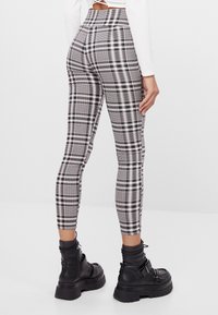 Legginsy w czarno-białą kratę z wysokim stanem. Gładki materiał o dopasowanym kroju, zestawione z masywnymi czarnymi botkami za kostkę.