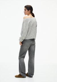 Maglione in misto lana grigio, design off-the-shoulder, abbinato a jeans in denim grigio a vita alta. Texture morbida e vestibilità comoda.