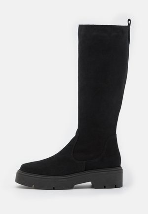 Botte haute en daim noir avec semelle épaisse en caoutchouc et petit talon, équipée d'une languette à l'arrière pour un enfilage facile.
