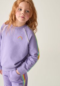 Lila Sweatshirt mit einem kleinen gestickten Regenbogenlogo, dekoriert mit bunten Streifenakzenten an den Ärmeln, aus einem weichen Stoff gefertigt.