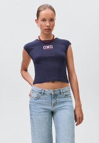 Mornarski crop top od mekog materijala s kratkim rukavima i ružičastim "OMG" grafikom. Uparen sa svijetloplavim širokim trapericama.
