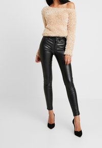 Béžový načechraný svetr s odkrytými rameny zkombinovaný s přiléhavými černými koženými kalhotami a černými lodičkami, které zdůrazňují kontrast textur.